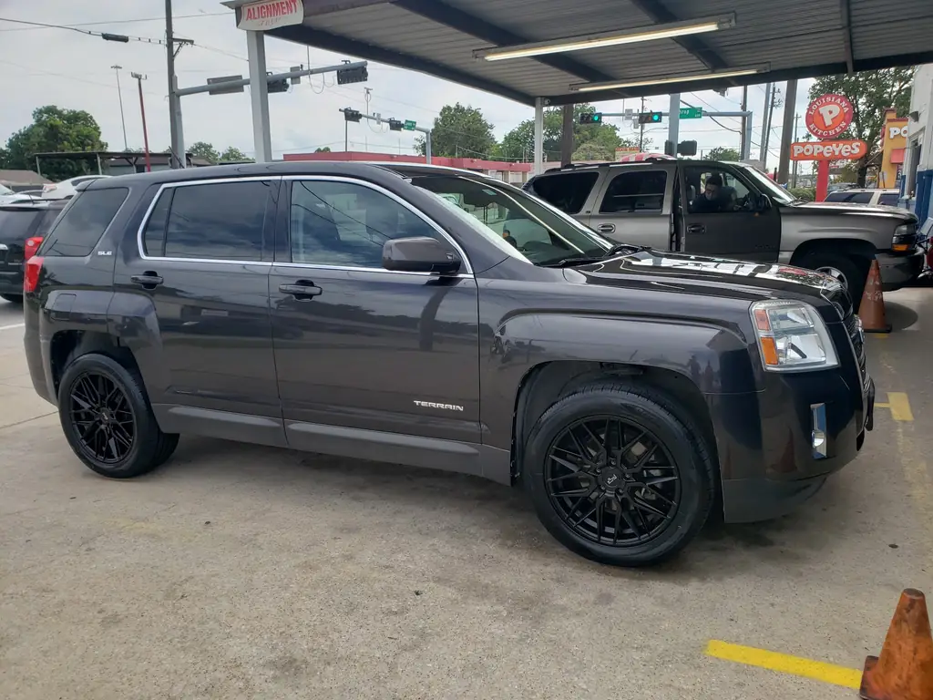 A GMC Terrain with black aftermarket wheels parked under the shop canopy beneath the Alignment sign
