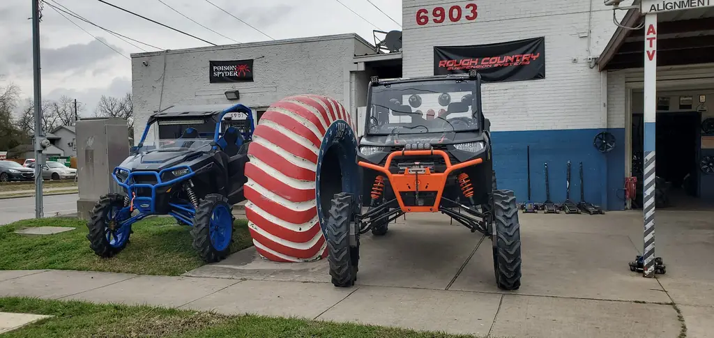 Two custom Polaris off-road buggies on oversized tires parked outside the D H Tire shop, with ATV alignment signage on the wall